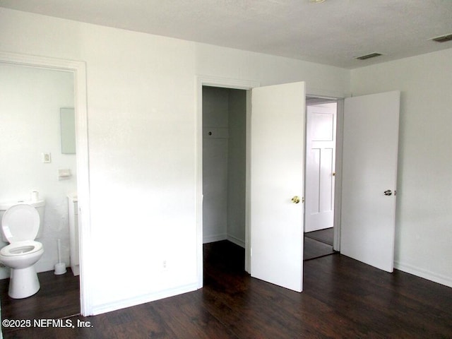 unfurnished bedroom with connected bathroom, a closet, and dark wood-type flooring