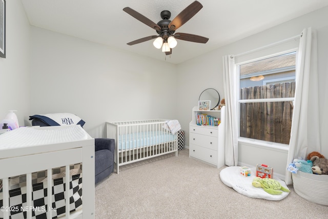 carpeted bedroom with ceiling fan and a crib