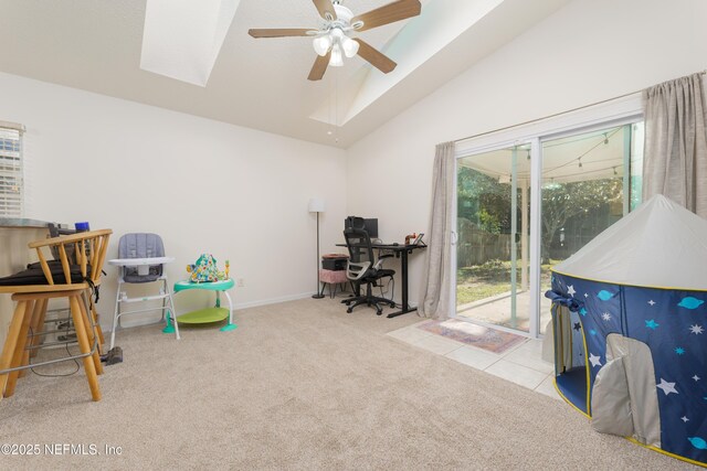 home office featuring ceiling fan, vaulted ceiling with skylight, and light carpet