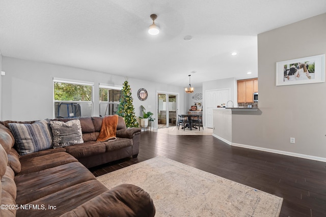 living room featuring dark wood-type flooring, sink, an inviting chandelier, and a textured ceiling