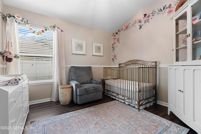 bedroom with a crib and dark wood-type flooring