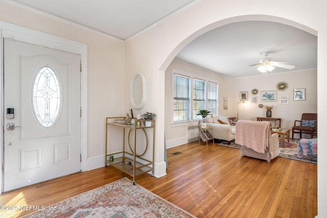 foyer entrance with hardwood / wood-style floors, ceiling fan, crown molding, and radiator