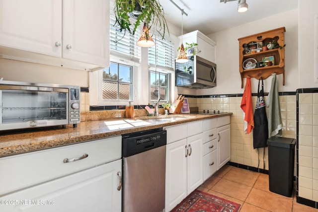 kitchen with sink, stainless steel appliances, light tile patterned floors, white cabinets, and tile walls