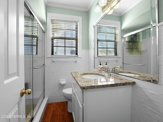 bathroom featuring toilet, crown molding, vanity, tile walls, and a shower with door