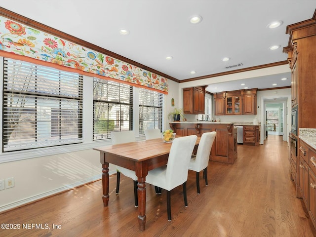 dining room with light wood-type flooring and crown molding