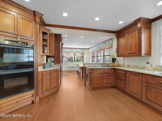 kitchen featuring black double oven, light stone counters, light hardwood / wood-style floors, kitchen peninsula, and crown molding