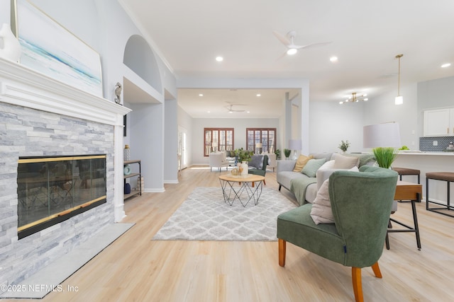 living room with ceiling fan, a stone fireplace, and light wood-type flooring