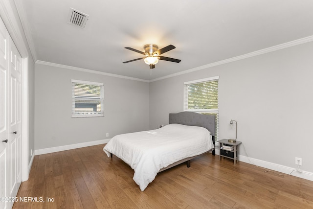 bedroom featuring ceiling fan, multiple windows, hardwood / wood-style flooring, a closet, and ornamental molding