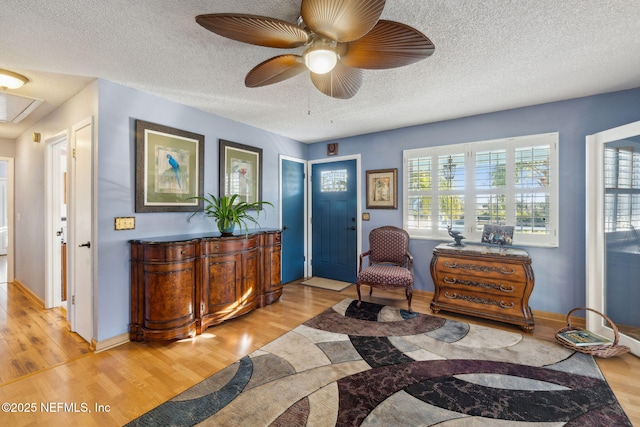 living area with ceiling fan, light hardwood / wood-style flooring, and a textured ceiling