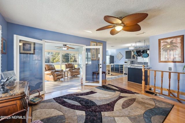 living room featuring french doors, a textured ceiling, light hardwood / wood-style flooring, and ceiling fan