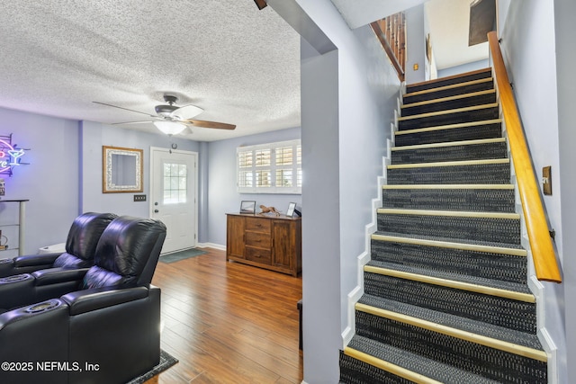 staircase with ceiling fan, wood-type flooring, and a textured ceiling