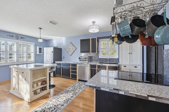 kitchen featuring a center island, stainless steel appliances, pendant lighting, light hardwood / wood-style floors, and decorative backsplash