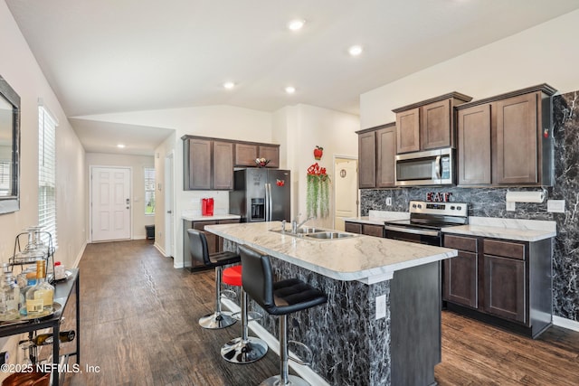 kitchen featuring decorative backsplash, appliances with stainless steel finishes, vaulted ceiling, a kitchen island with sink, and sink