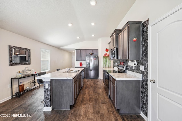 kitchen featuring sink, dark hardwood / wood-style flooring, lofted ceiling, a kitchen island with sink, and appliances with stainless steel finishes