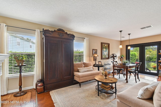 living room with a wealth of natural light, a textured ceiling, and light wood-type flooring