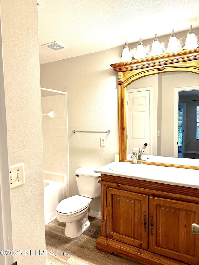 full bathroom with tiled shower / bath combo, a textured ceiling, toilet, vanity, and hardwood / wood-style flooring