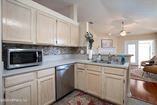 kitchen with sink, vaulted ceiling, appliances with stainless steel finishes, kitchen peninsula, and backsplash