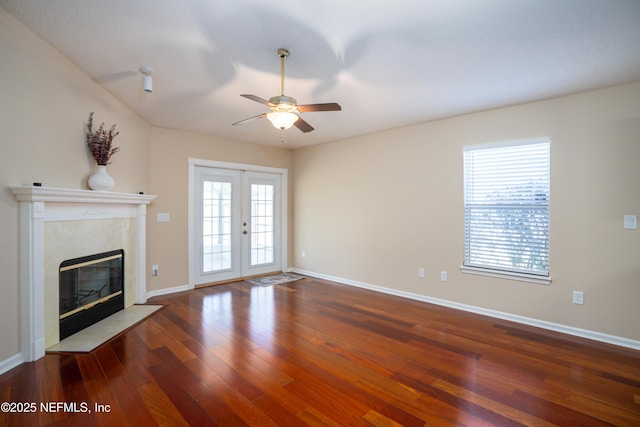 unfurnished living room with french doors, a premium fireplace, ceiling fan, wood finished floors, and baseboards