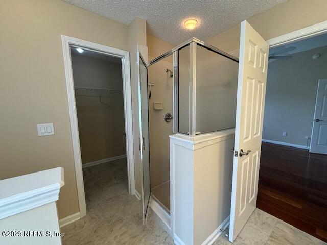 full bath featuring a textured ceiling, a spacious closet, a shower stall, and baseboards