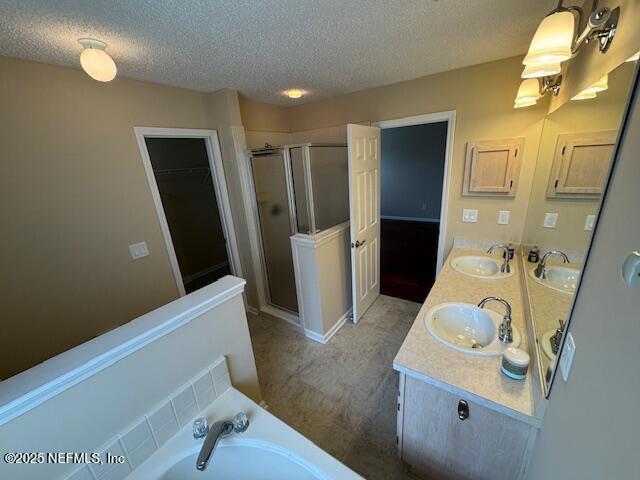 bathroom with a textured ceiling, double vanity, a stall shower, and a sink