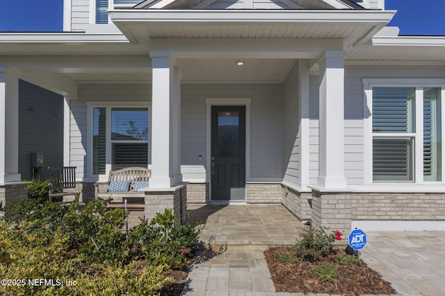 doorway to property featuring covered porch and brick siding