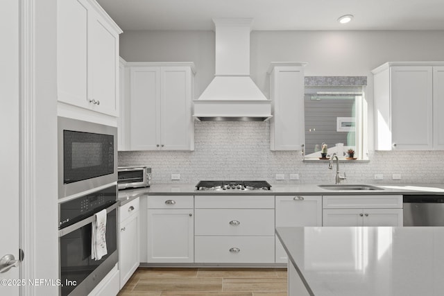 kitchen featuring stainless steel appliances, custom range hood, white cabinetry, and tasteful backsplash