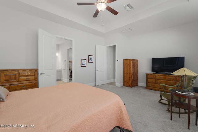 carpeted bedroom featuring a raised ceiling, ensuite bath, and ceiling fan