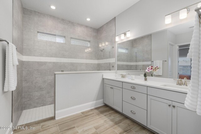 bathroom featuring wood finish floors, double vanity, a sink, and walk in shower