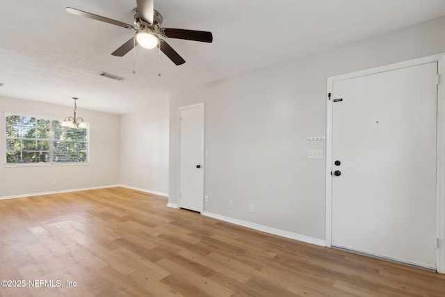 spare room with ceiling fan with notable chandelier and light hardwood / wood-style flooring