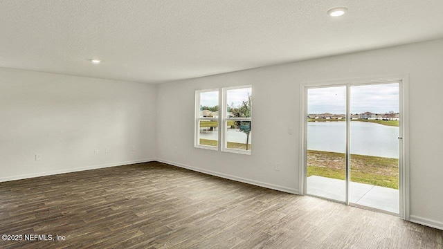 spare room featuring dark hardwood / wood-style floors, a water view, and a textured ceiling