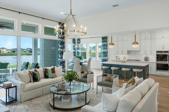 living room featuring light wood-type flooring, a water view, an inviting chandelier, and ornamental molding