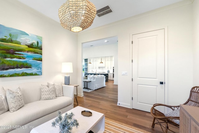 living room with wood-type flooring, ornamental molding, and an inviting chandelier