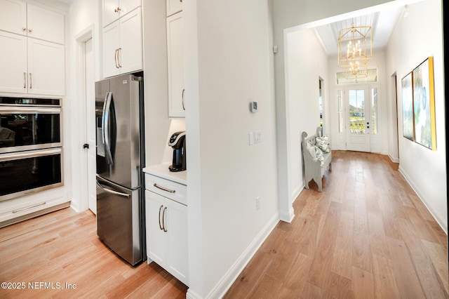 kitchen with decorative light fixtures, stainless steel appliances, white cabinetry, and light hardwood / wood-style flooring