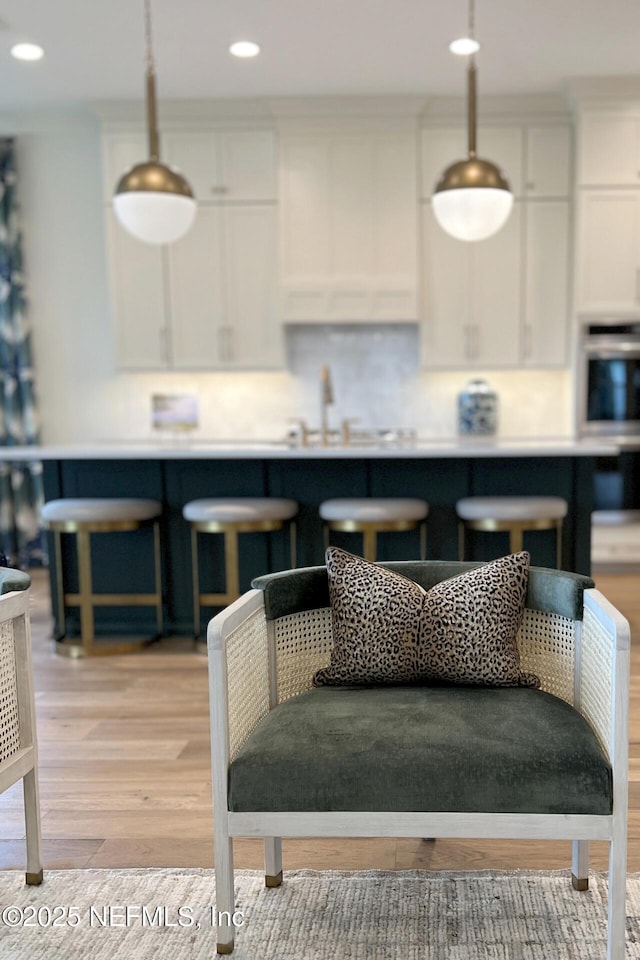 kitchen featuring light wood-type flooring, backsplash, stainless steel oven, white cabinets, and hanging light fixtures