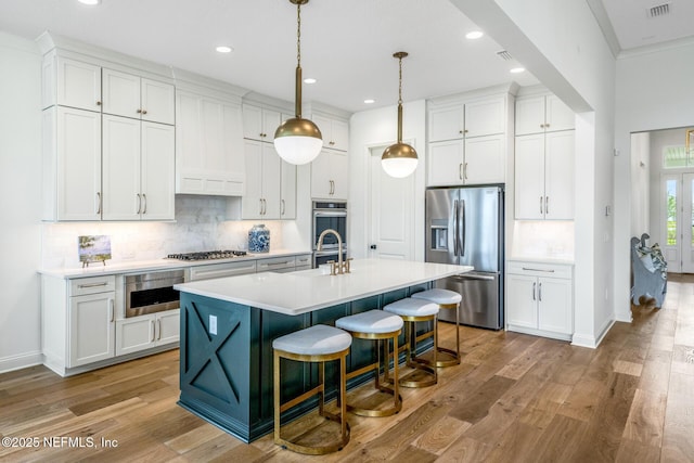 kitchen with a center island with sink, light hardwood / wood-style flooring, decorative light fixtures, white cabinetry, and stainless steel appliances