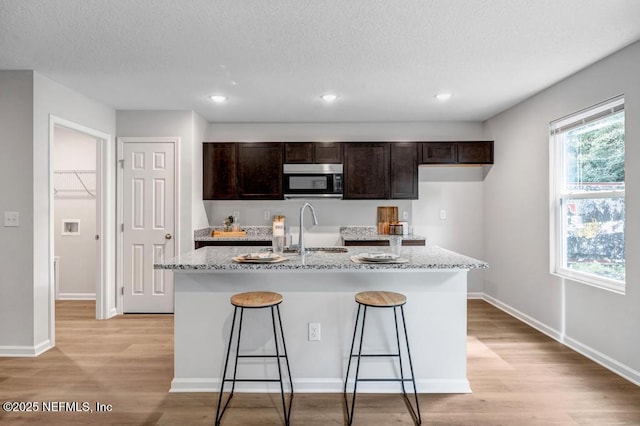 kitchen featuring light stone counters, a kitchen island with sink, a breakfast bar area, and sink