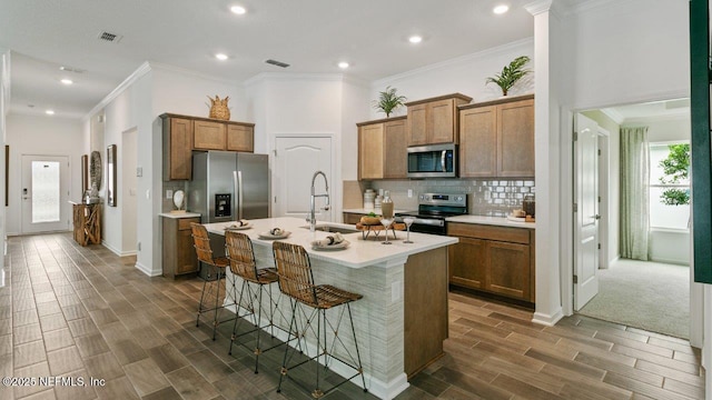 kitchen with a kitchen breakfast bar, sink, crown molding, an island with sink, and appliances with stainless steel finishes