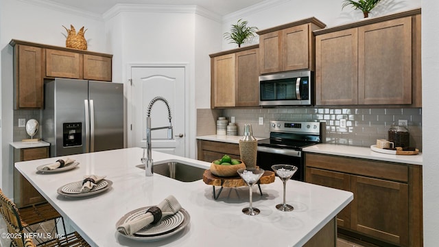 kitchen with sink, stainless steel appliances, a kitchen island with sink, a breakfast bar, and ornamental molding