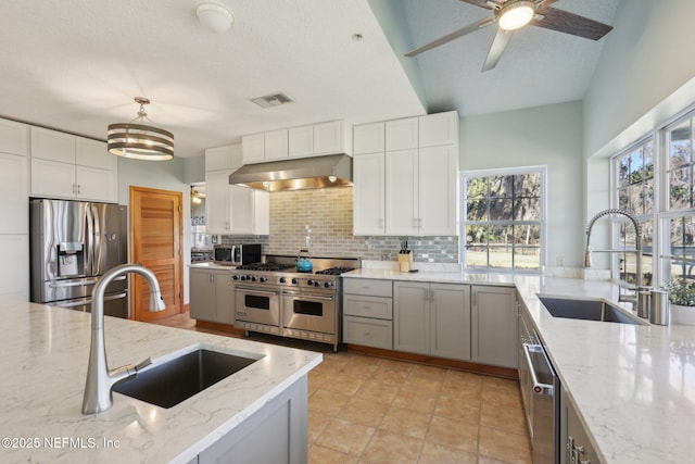 kitchen with light stone counters, sink, decorative light fixtures, and stainless steel appliances