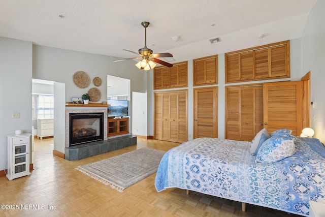 bedroom with ceiling fan, a towering ceiling, a fireplace, parquet flooring, and multiple closets