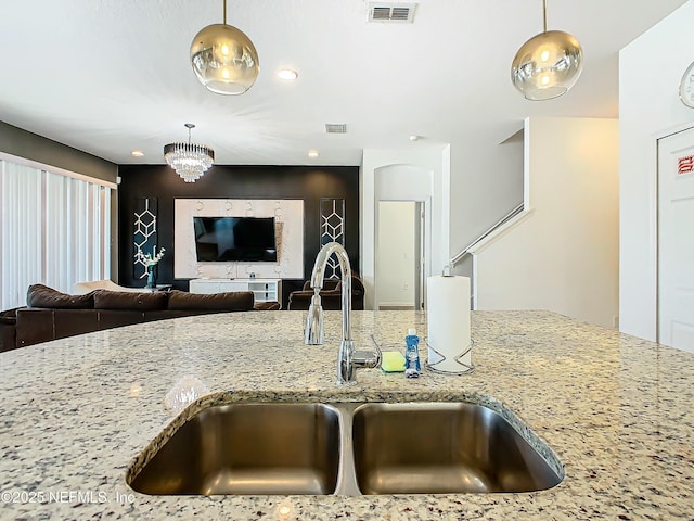 kitchen with decorative light fixtures, light stone counters, and sink