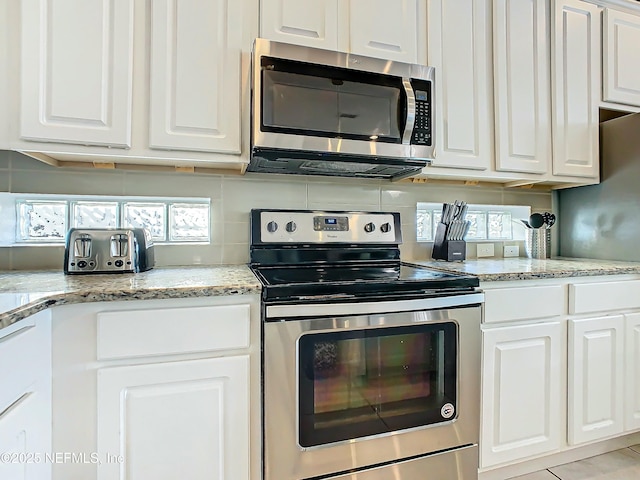 kitchen with light stone countertops, white cabinets, light tile patterned floors, and appliances with stainless steel finishes