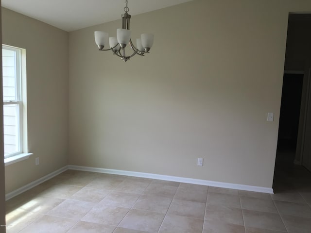 empty room with light tile patterned flooring and a chandelier