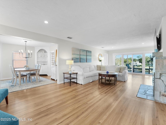 living room with a textured ceiling, light hardwood / wood-style flooring, built in features, and a notable chandelier