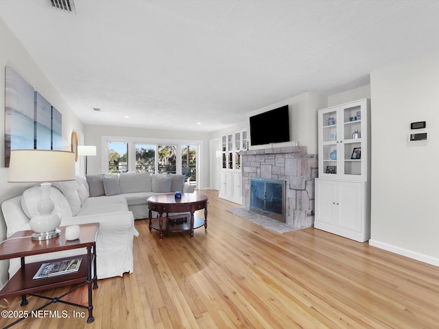 living room with light wood-type flooring, built in features, and a stone fireplace