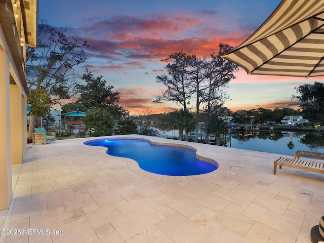 pool at dusk featuring a patio and a water view