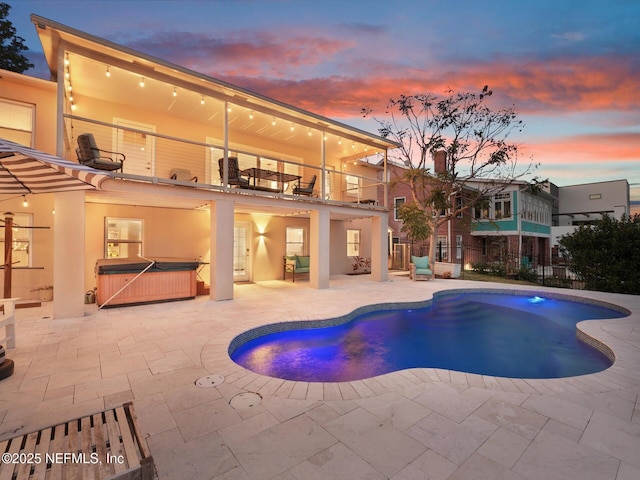 pool at dusk featuring a hot tub and a patio