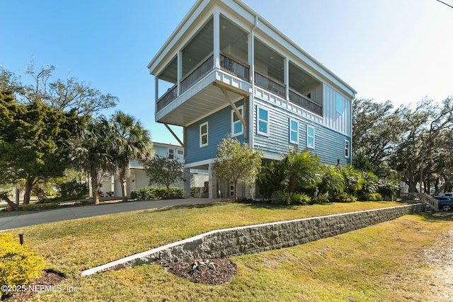 beach home featuring a balcony, driveway, and a yard