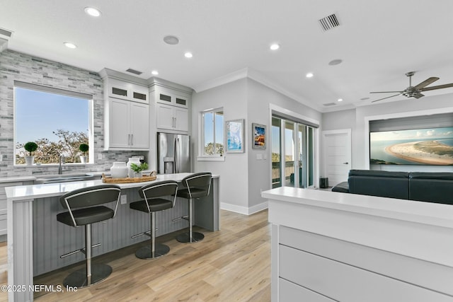 kitchen with stainless steel fridge, white cabinets, glass insert cabinets, light countertops, and a sink