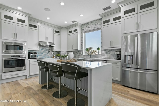 kitchen featuring a kitchen island, appliances with stainless steel finishes, light countertops, under cabinet range hood, and a kitchen bar